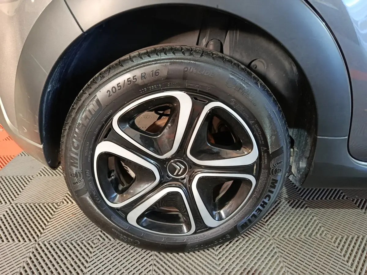 Gros plan sur la roue avant gauche d'une Citroën C3 gris foncé, avec jante noire et inserts argentés distinctifs.