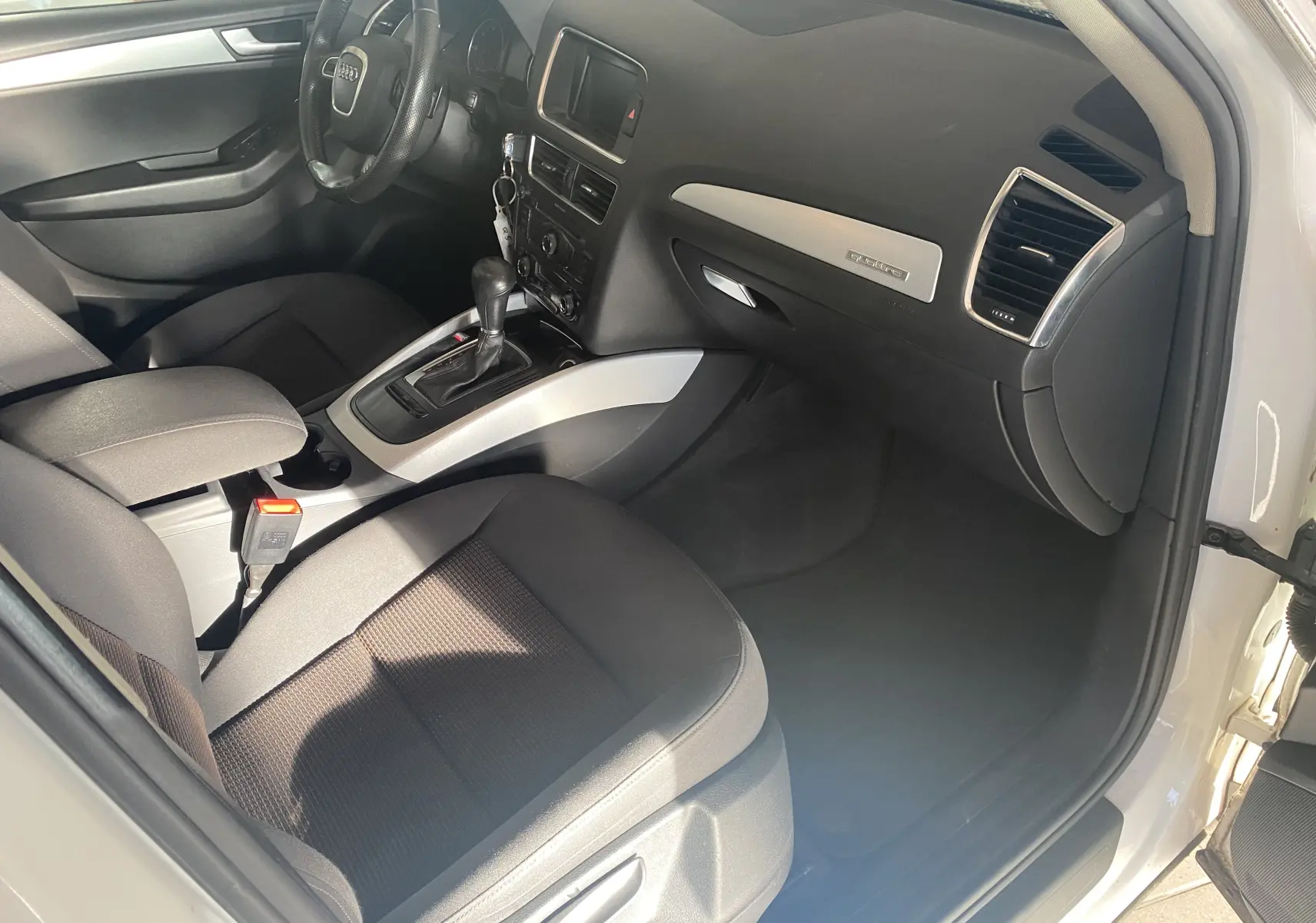 Intérieur avant droit d'un Audi Q5 blanc 2012, avec tableau de bord noir et inserts argentés, volant multifonction visible.
