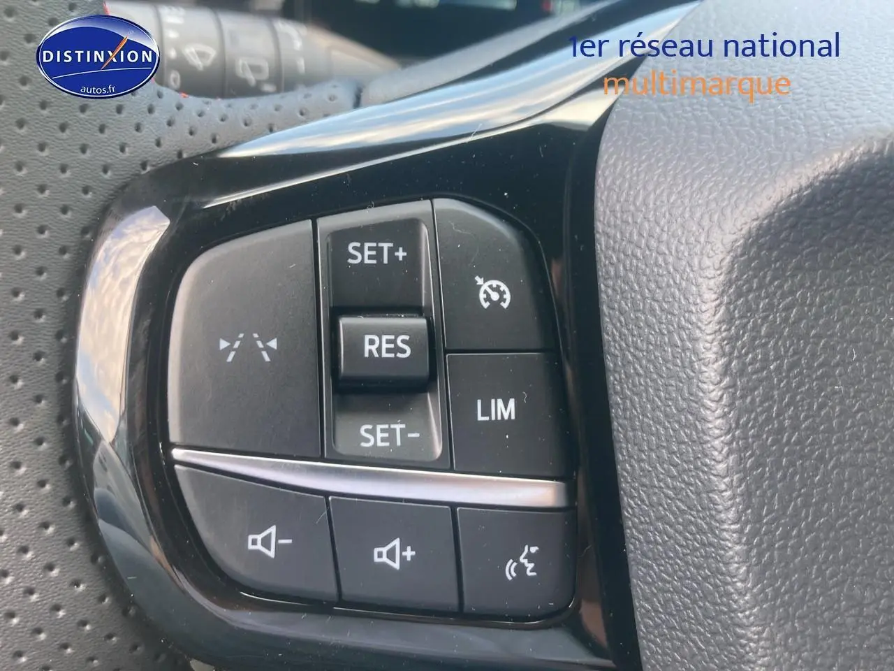 Gros plan sur les commandes du régulateur de vitesse et du volume sur le volant perforé d'un Ford Puma gris cactus.