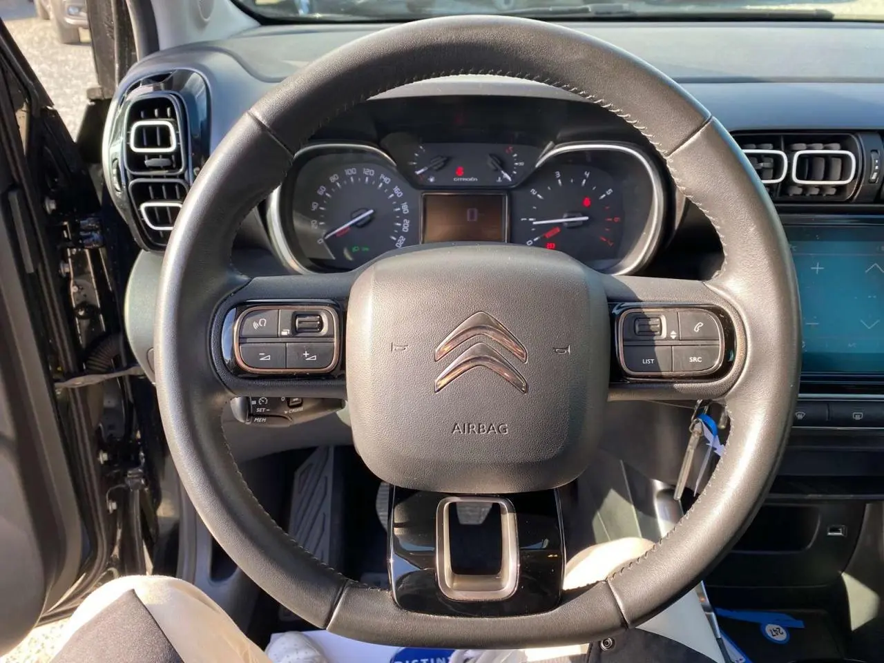Vue rapprochée du volant en croûte de cuir d'une Citroën C3 Aircross noire, avec tableau de bord et commandes au volant visibles.
