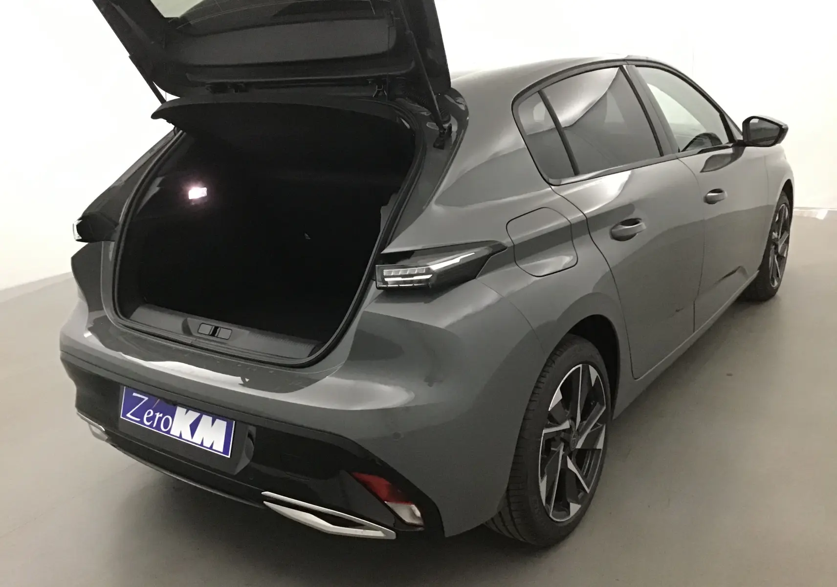 Peugeot 308 gris Sellenium vue 3/4 arrière droit avec coffre ouvert et jantes alliage noires.