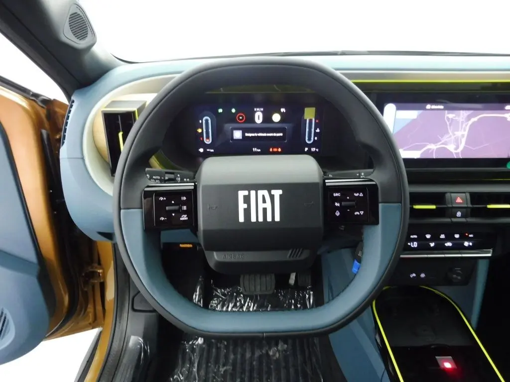 Vue rapprochée du volant noir et bleu avec logo FIAT, tableau de bord digital et intérieur bronze Luna de la Grande Panda 2025.