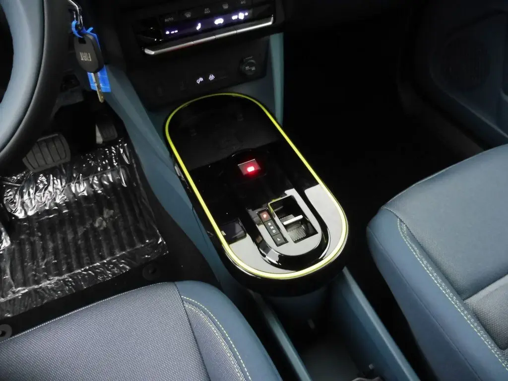 Gros plan sur la console centrale noire avec liseré jaune de la FIAT Grande Panda 2025, sièges tissu bleu visible.