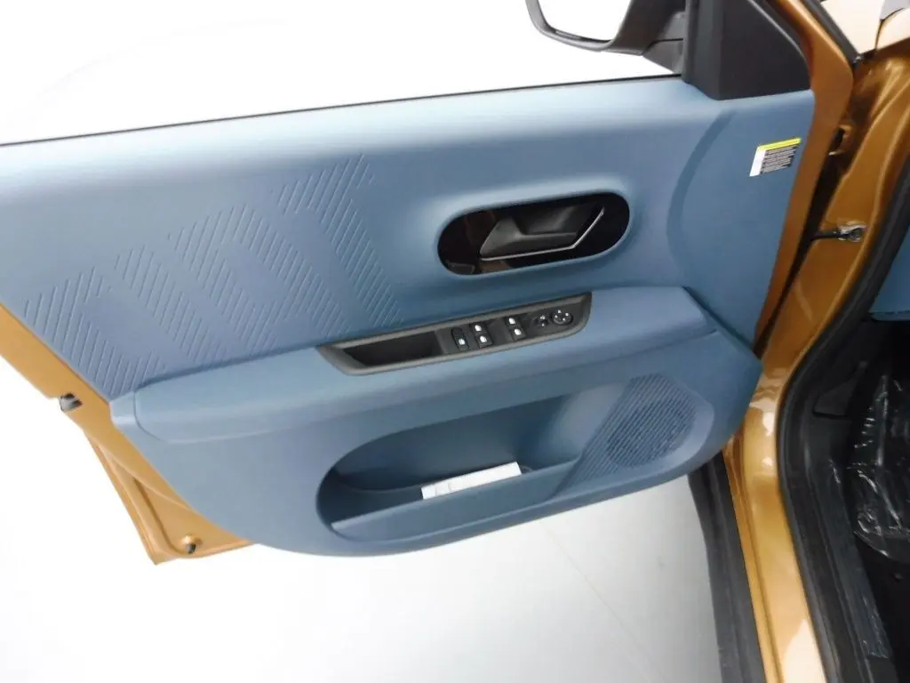 Vue intérieure côté gauche de la porte avant d'une Fiat Grande Panda 2025 bronze luna avec panneau bleu et commandes électriques.