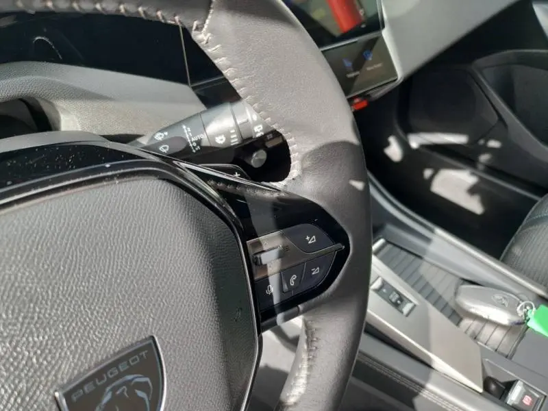 Gros plan sur le volant multifonction noir de la Peugeot 308 2024, avec commandes audio et téléphone intégrées.
