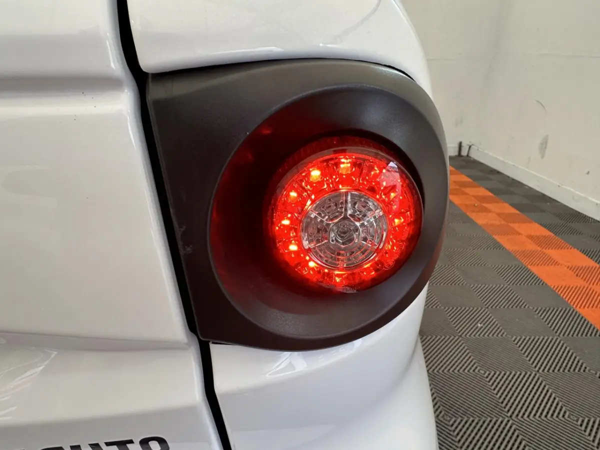 Gros plan sur le feu arrière droit rouge d’une Aixam Minauto E Access blanche, avec carrosserie et sol à damiers orange et gris.