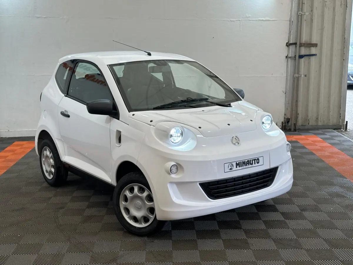 Vue 3/4 avant droite d'une Aixam Minauto E Access blanche avec phares ronds et rétroviseur caméra côté conducteur.