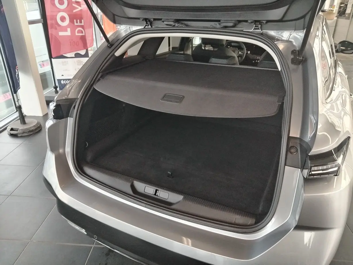 Coffre ouvert vu de l'arrière d'une Peugeot 308 SW Hybrid 145 gris Artense, montrant l'espace de chargement et la tablette cache-bagages.