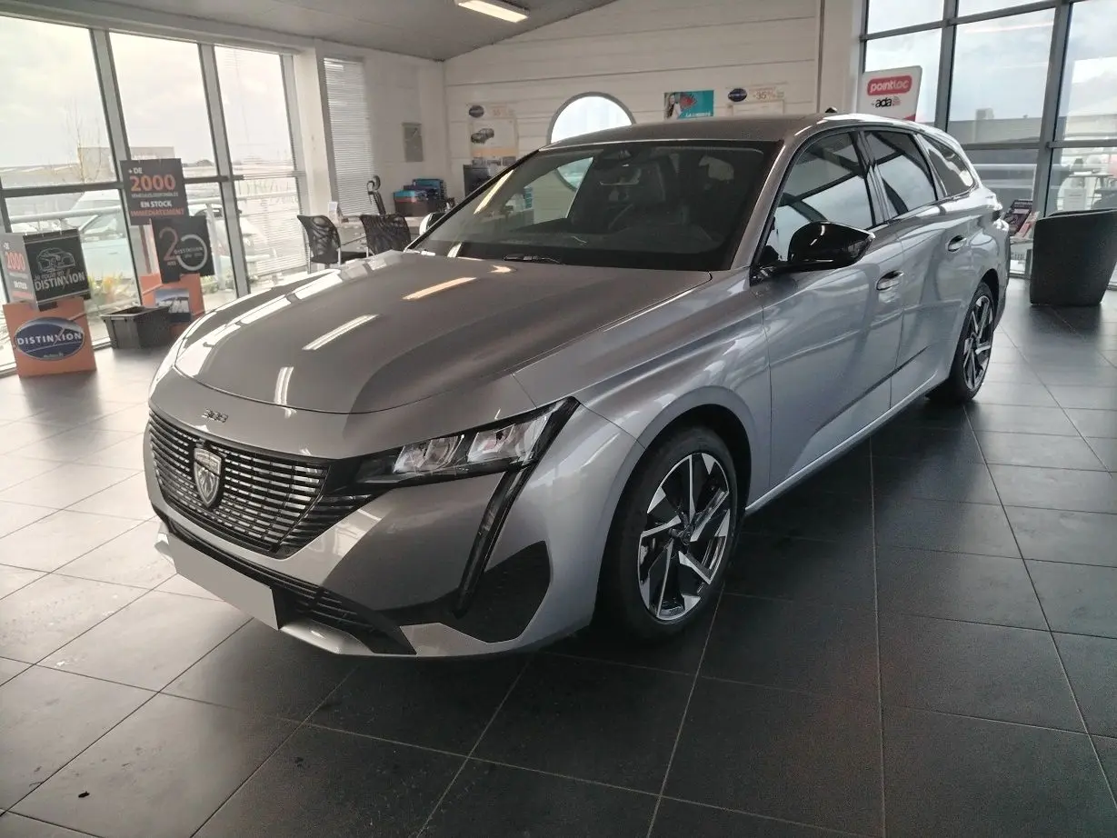 Peugeot 308 SW Hybrid gris Artense vue 3/4 avant droit en showroom avec jantes bi-ton et calandre distinctive.