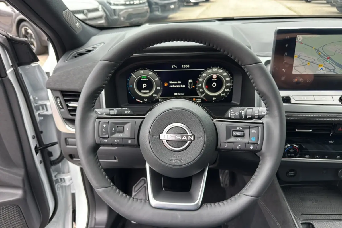 Vue intérieure centrée sur le volant cuir multifonctions d’un Nissan Qashqai blanc lunaire avec écran digital et navigation.