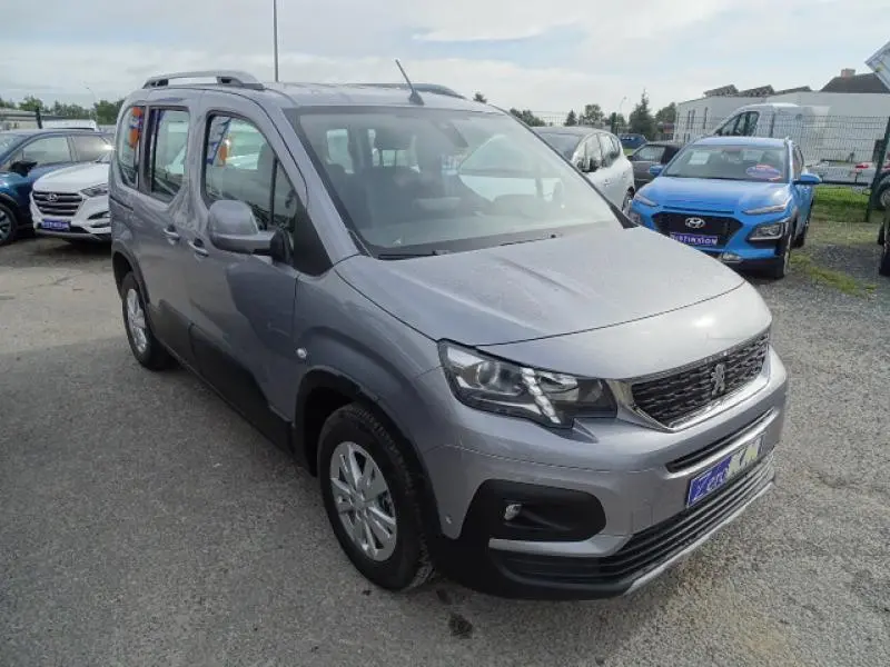 Peugeot Rifter gris Artense vu en 3/4 avant droit, avec calandre noire et toit surélevé, stationné en extérieur.