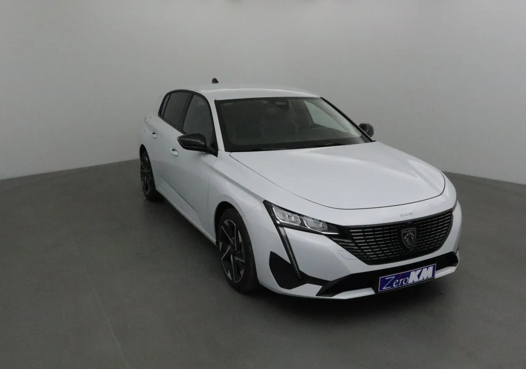 Peugeot 308 blanc Okenite vue 3/4 avant droit, avec calandre noire et feux LED distinctifs.