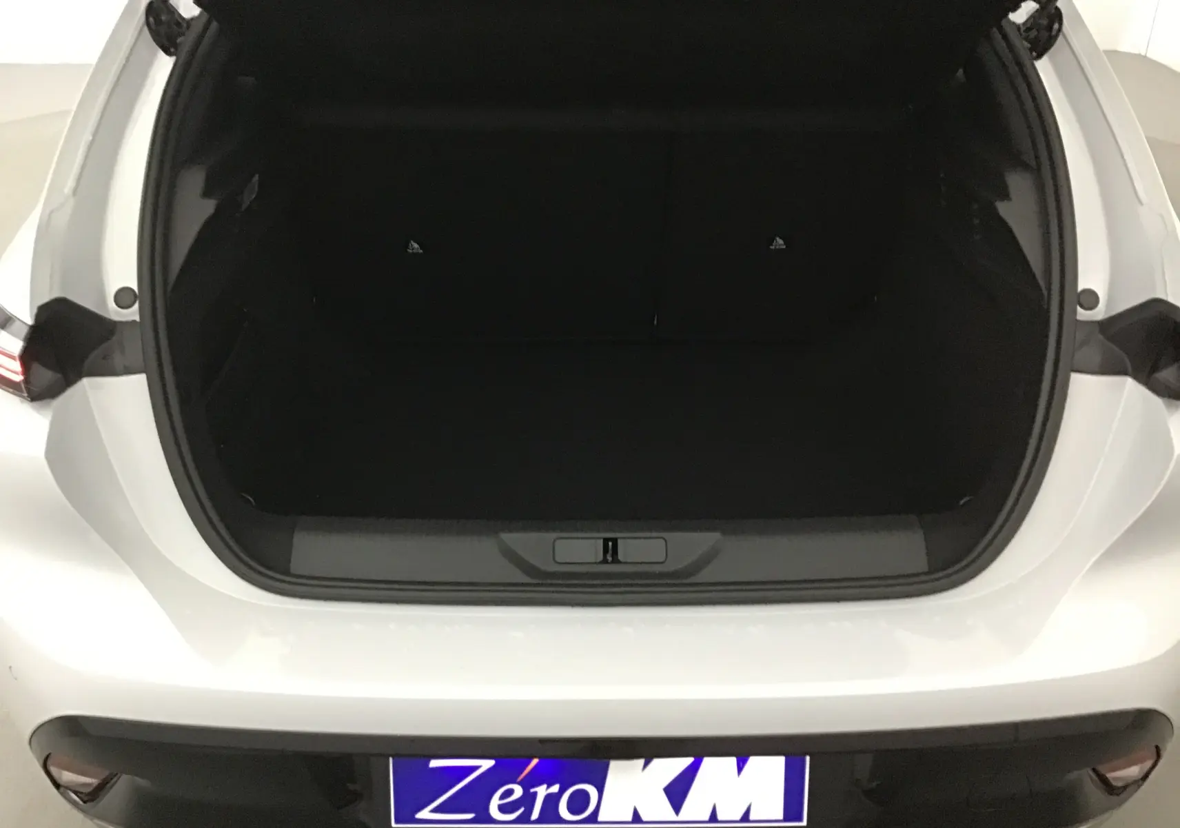 Coffre ouvert vu de l'arrière d'une Peugeot 308 blanche Okenite, version 2025 avec plaque Zéro KM visible.