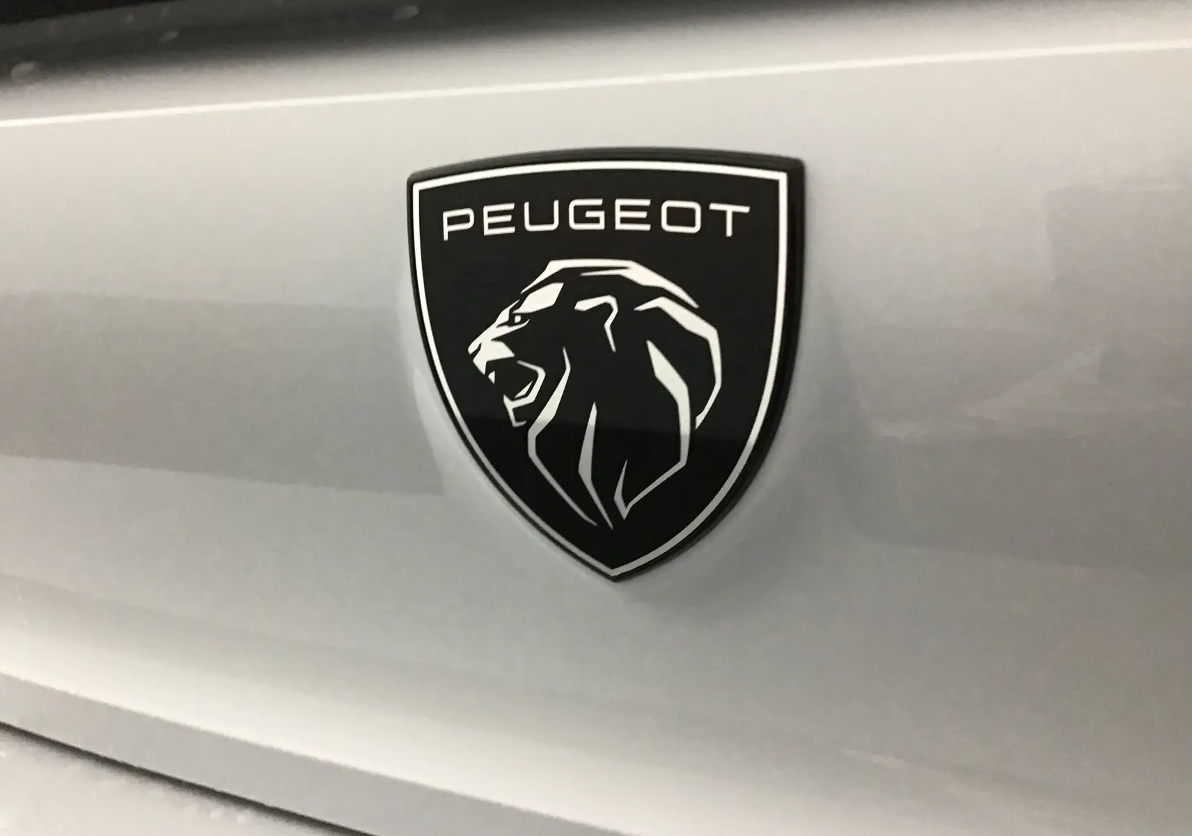 Gros plan sur l'emblème noir et blanc du lion Peugeot sur la carrosserie blanche Okenite du 308 2025.
