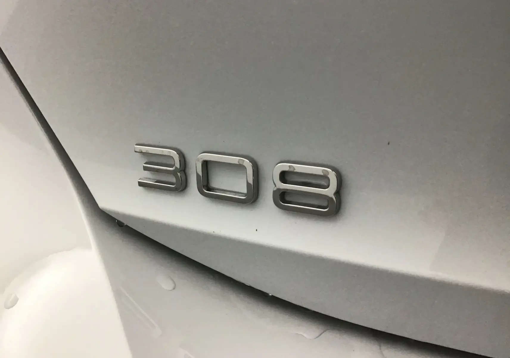 Gros plan sur l'emblème "308" en chrome sur la carrosserie blanche Okenite d'une Peugeot 308 2025.