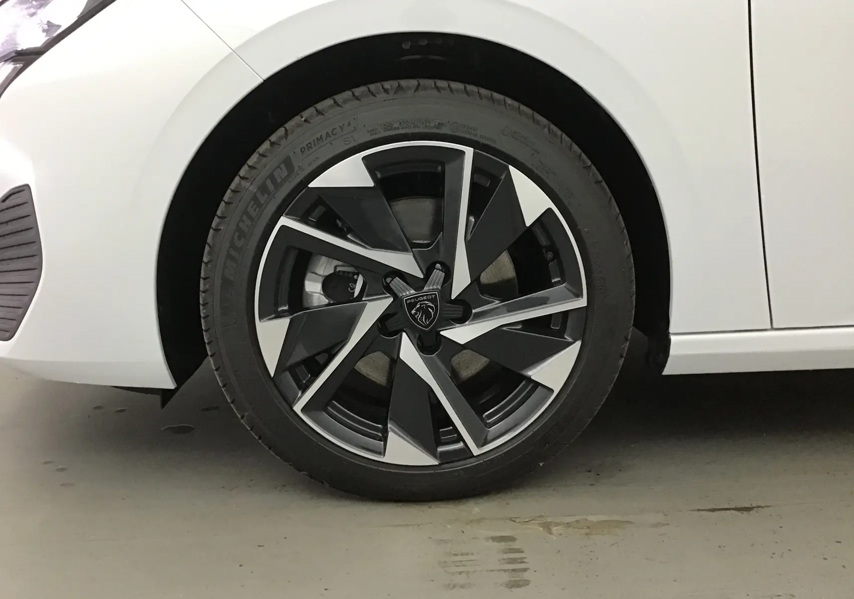 Gros plan sur la roue avant gauche d'une Peugeot 308 blanche Okenite avec jante alliage noire et argentée au design moderne.