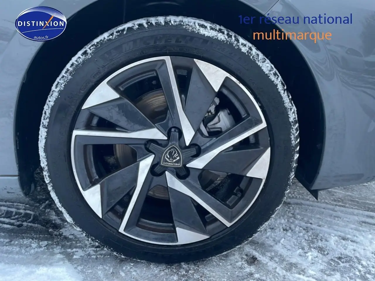 Gros plan sur la jante alu noire et argentée d'une Peugeot 308 gris sélénite, avec traces de neige autour du pneu.