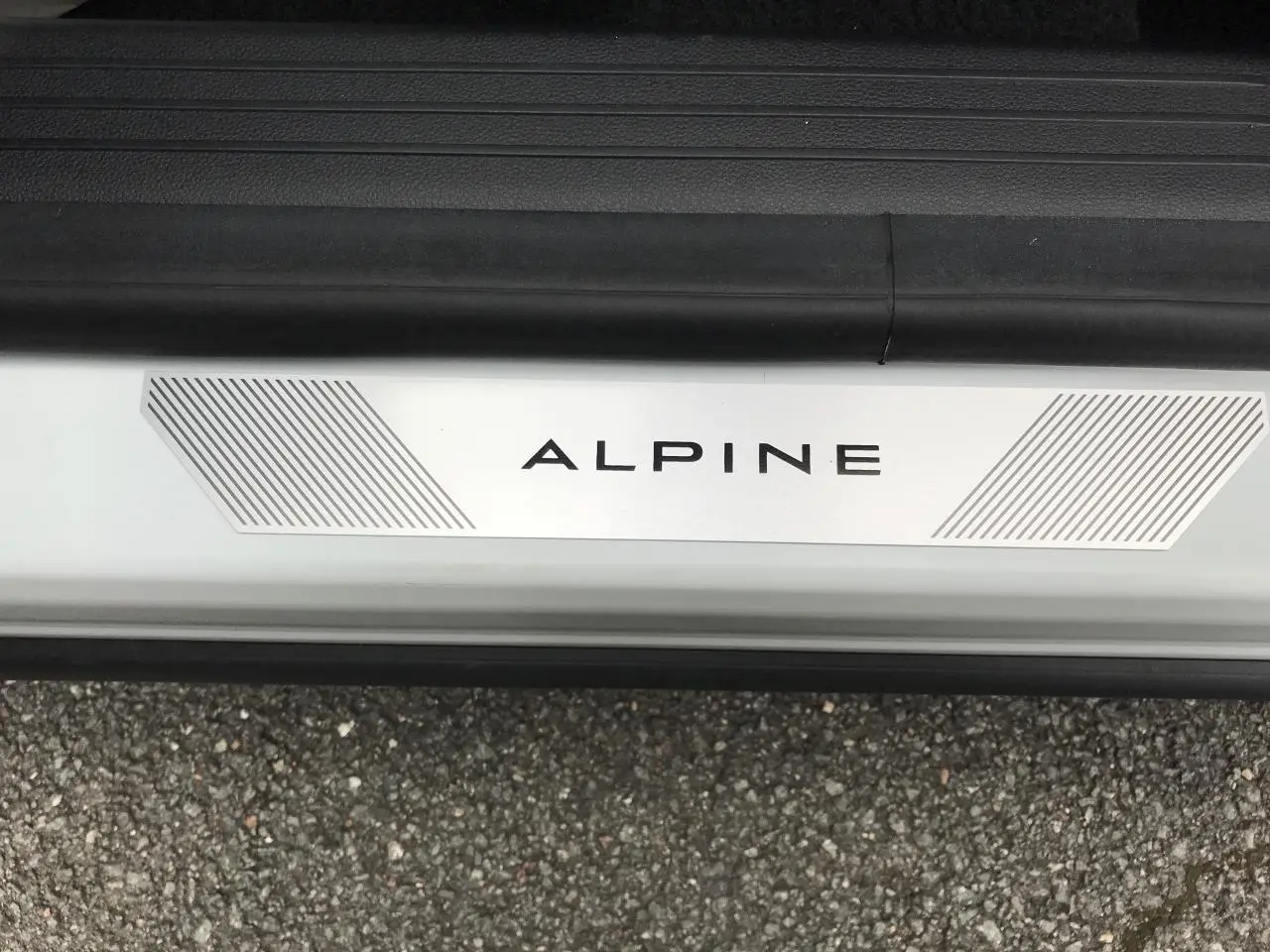 Gros plan sur le seuil de porte blanc du Renault Austral Esprit Alpine avec logo ALPINE et sol goudronné visible.