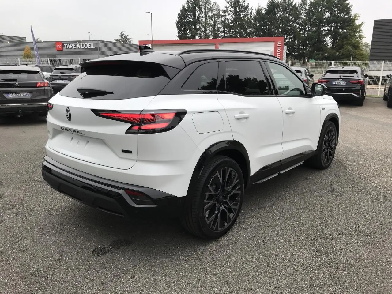 Vue 3/4 arrière droite du Renault Austral blanc bi-ton avec jantes noires et toit noir satin, stationné en extérieur.