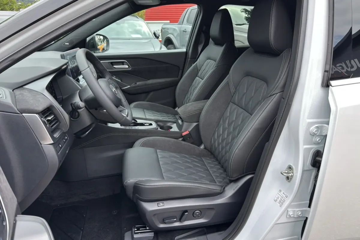 Vue intérieure côté conducteur du Nissan Qashqai blanc lunaire, sièges cuir noirs avec surpiqûres et console centrale visible.