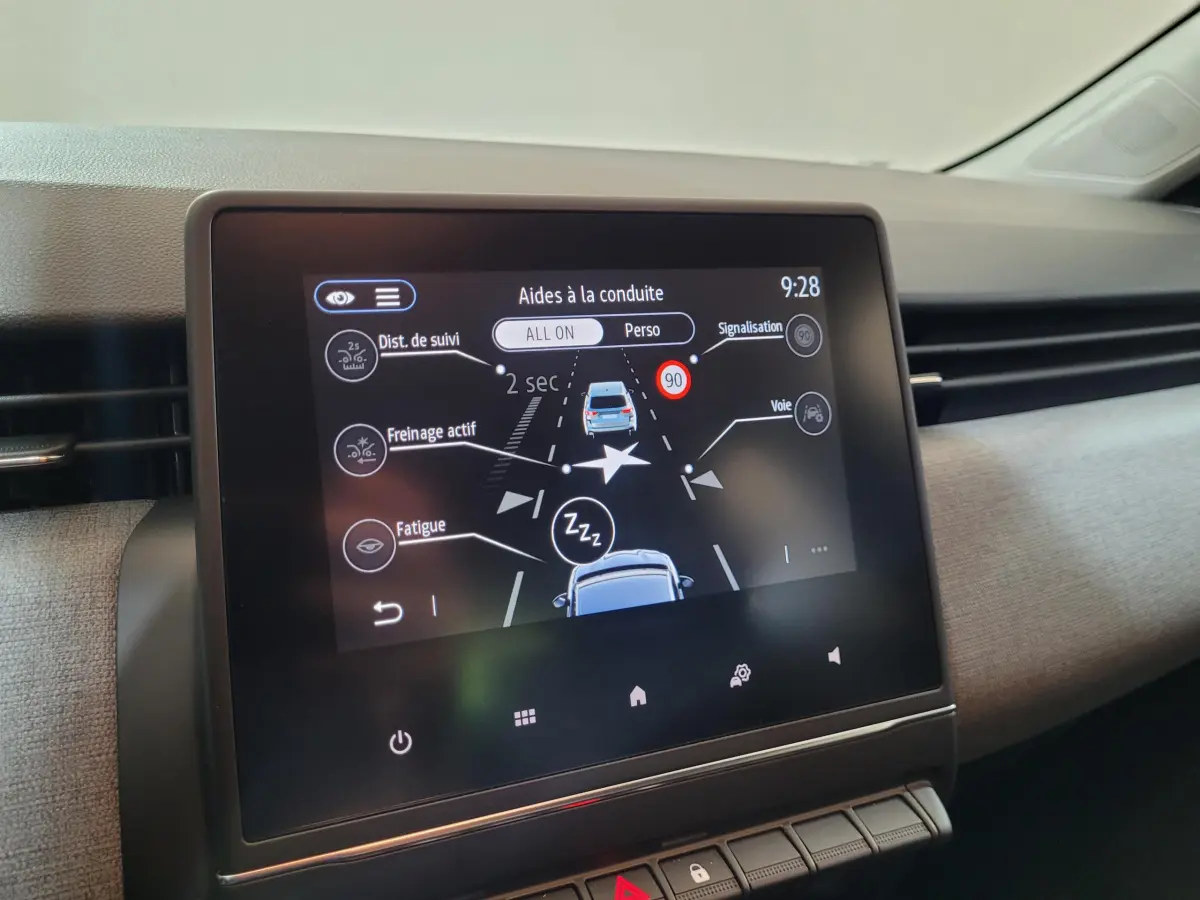 Écran tactile central affichant les aides à la conduite dans l’habitacle d’une Renault Clio gris foncé, vue de face.