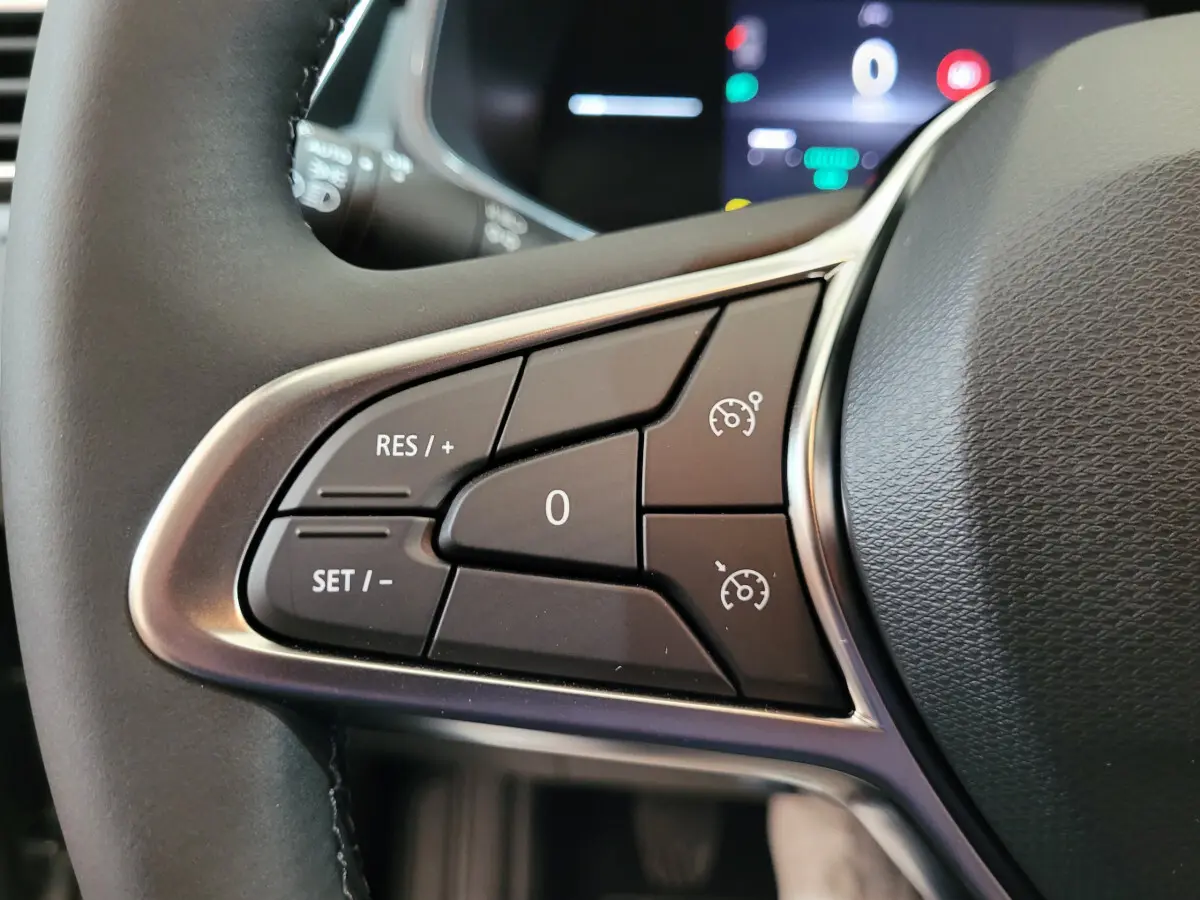 Gros plan sur les commandes du régulateur de vitesse au volant cuir d'une Renault Clio gris foncé, affichage numérique en arrière-plan.