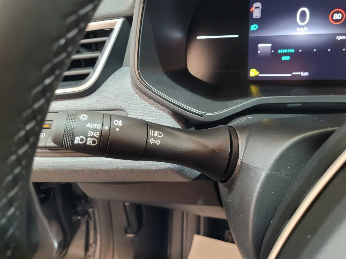 Gros plan sur la commande d’éclairage à gauche du volant dans l’habitacle gris foncé de la Renault Clio Evolution 2025.