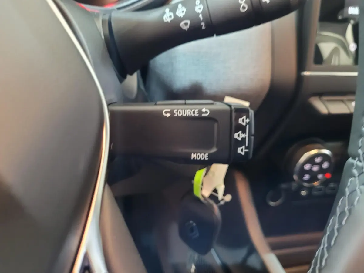 Gros plan sur la commande multifonction au volant d’une Renault Clio gris foncé, intérieur avec détails du tableau de bord.