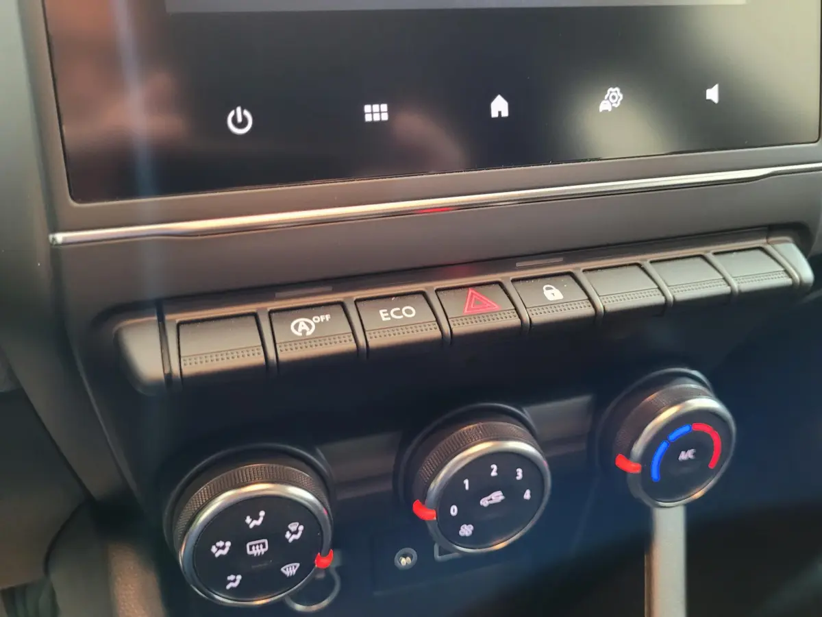 Gros plan sur la console centrale de la Renault Clio gris foncé, montrant les commandes de climatisation et les boutons multifonctions.