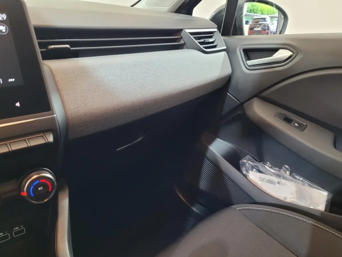 Vue intérieure côté passager de la Renault Clio gris foncé 2025, avec tableau de bord textile et commandes climatisation.