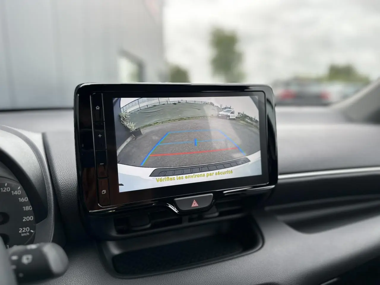 Écran tactile central affichant la caméra de recul d'une Toyota Yaris blanche, vue intérieure du tableau de bord.