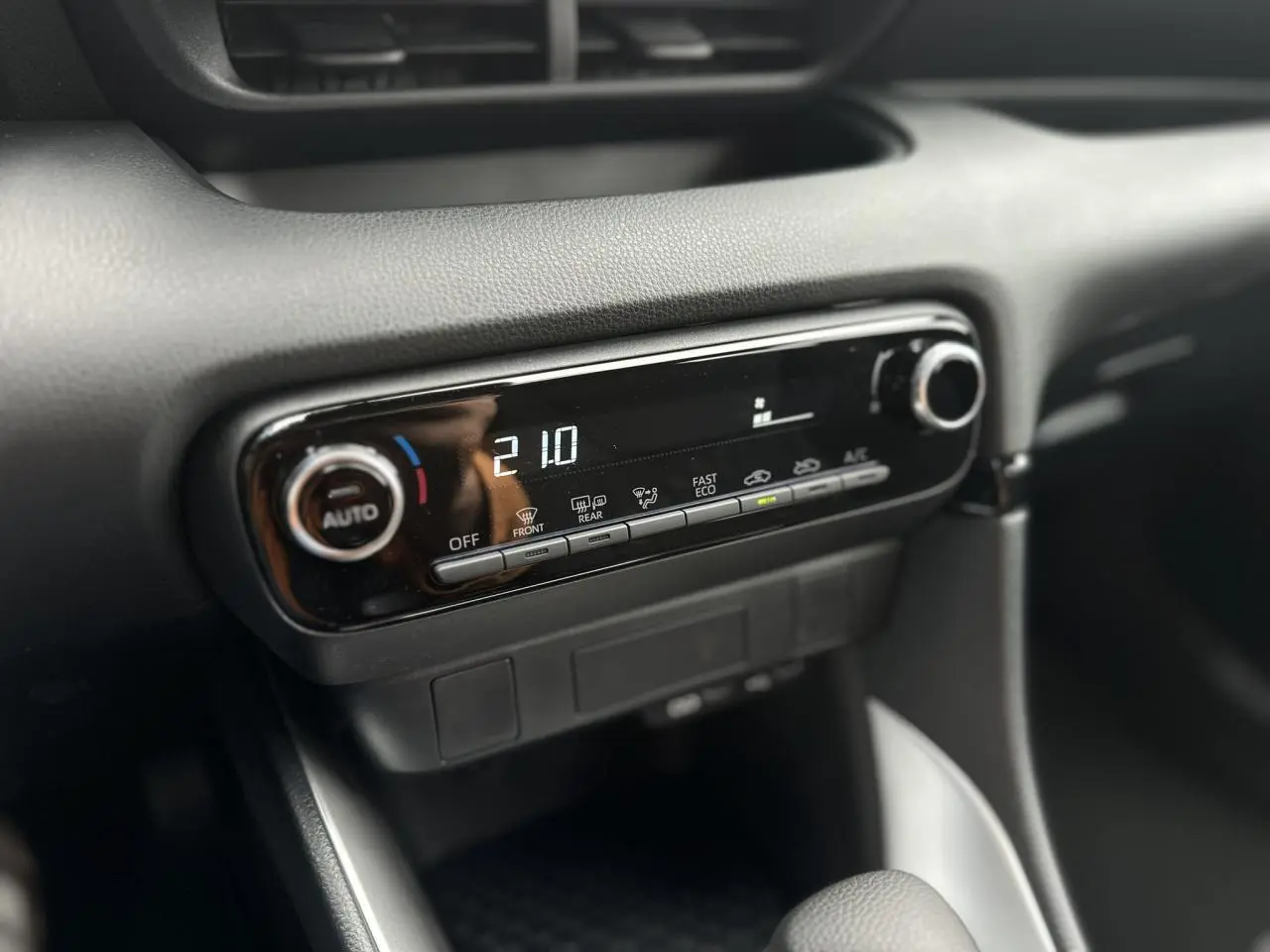 Gros plan sur la console centrale noire de la Toyota Yaris hybride 2025, affichant la climatisation automatique à 21°C.
