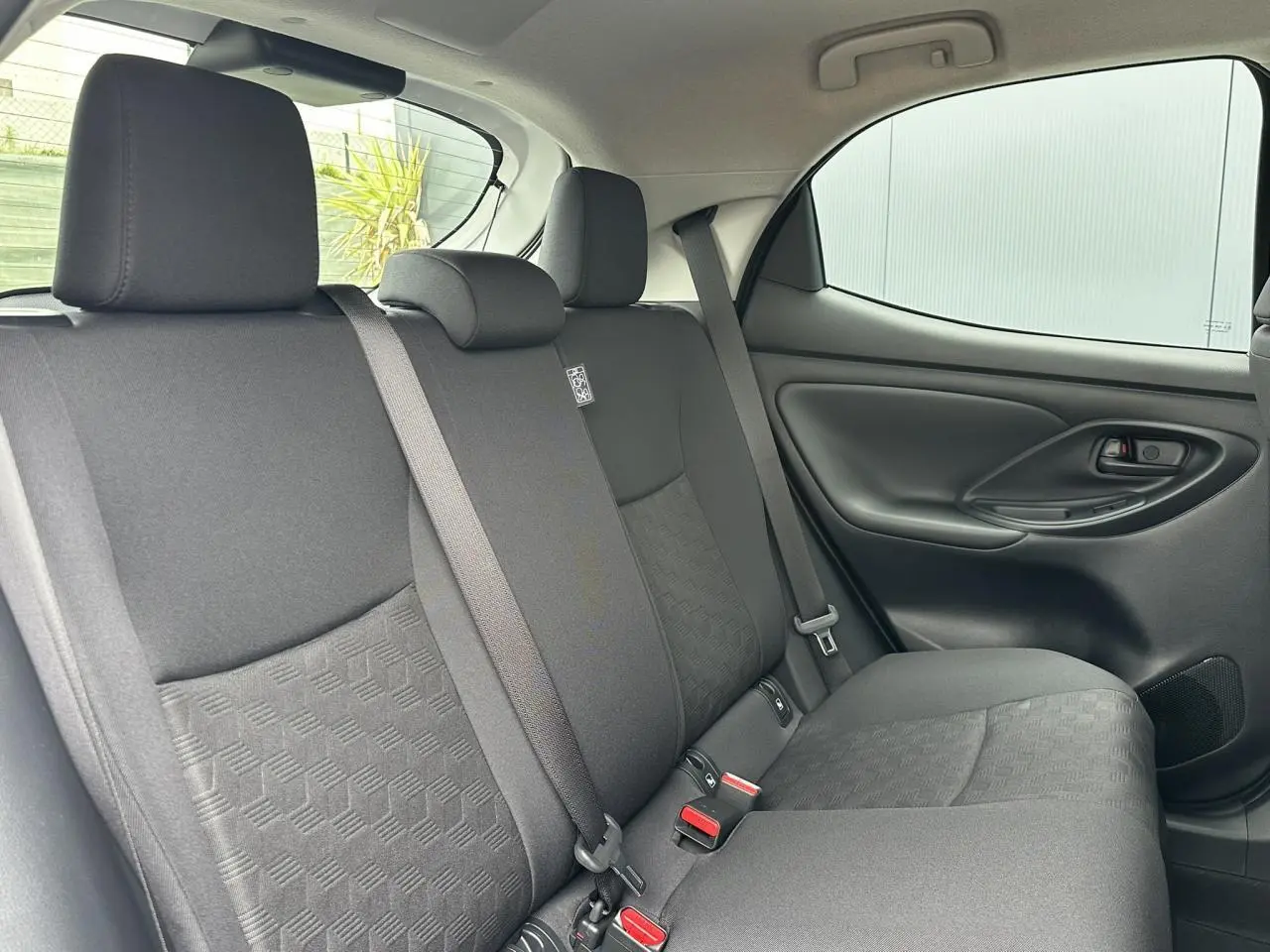 Vue intérieure arrière droite des sièges arrière en tissu noir de la Toyota Yaris Hybride 2025, avec ceinture de sécurité visible.