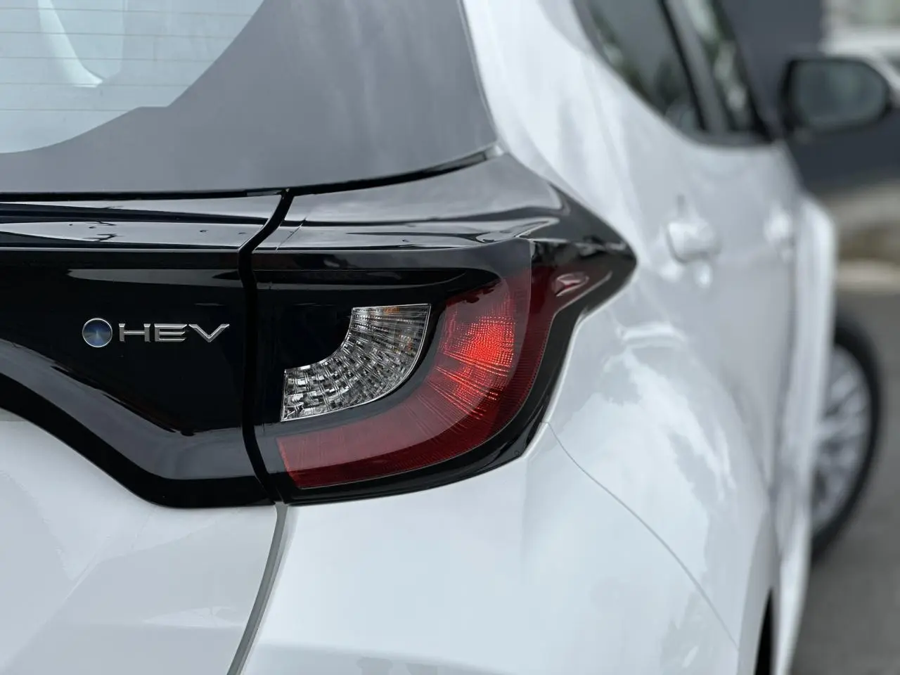 Gros plan sur le feu arrière droit et l'inscription HEV d'une Toyota Yaris hybride blanche vue de l'arrière.