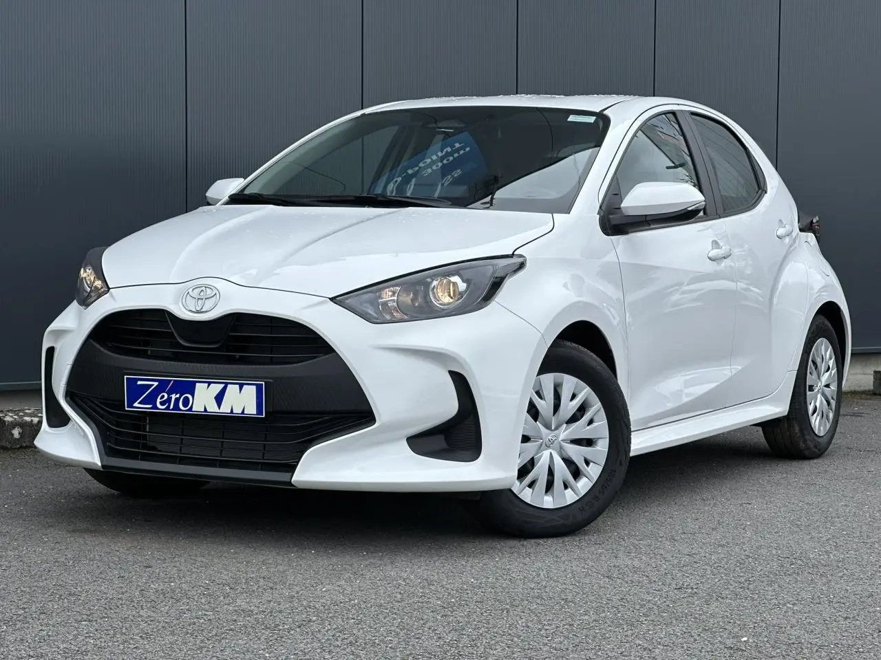 Toyota Yaris hybride blanc pur vue 3/4 avant droit avec calandre noire et jantes tôles à enjoliveurs.