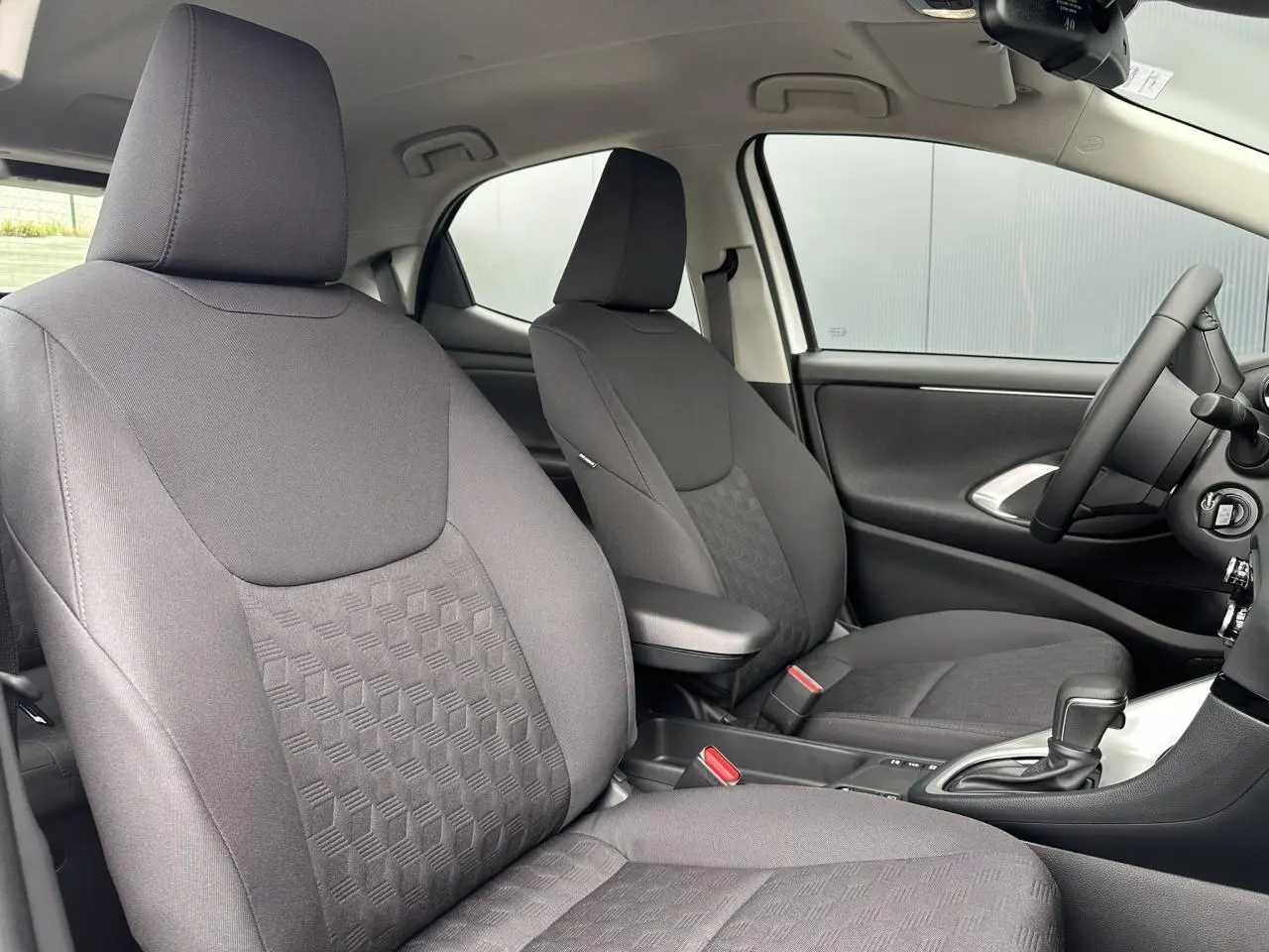 Intérieur de la Toyota Yaris Hybride 2025 vu côté droit, sièges tissu noir avec accoudoir central et boîte auto.