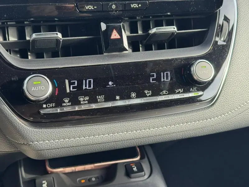 Gros plan sur la console centrale de la Toyota Corolla 2025, affichant la climatisation automatique bi-zone à 21°C.