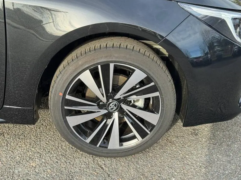 Gros plan sur la roue avant gauche noire d'une Toyota Corolla 2025 avec jante alliage bicolore et partie avant du véhicule visible.