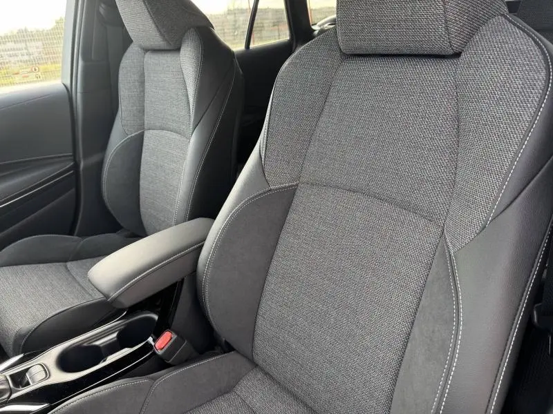 Gros plan sur les sièges avant gris tissu et cuir de la Toyota Corolla 2025, avec accoudoir central et console noire brillante.