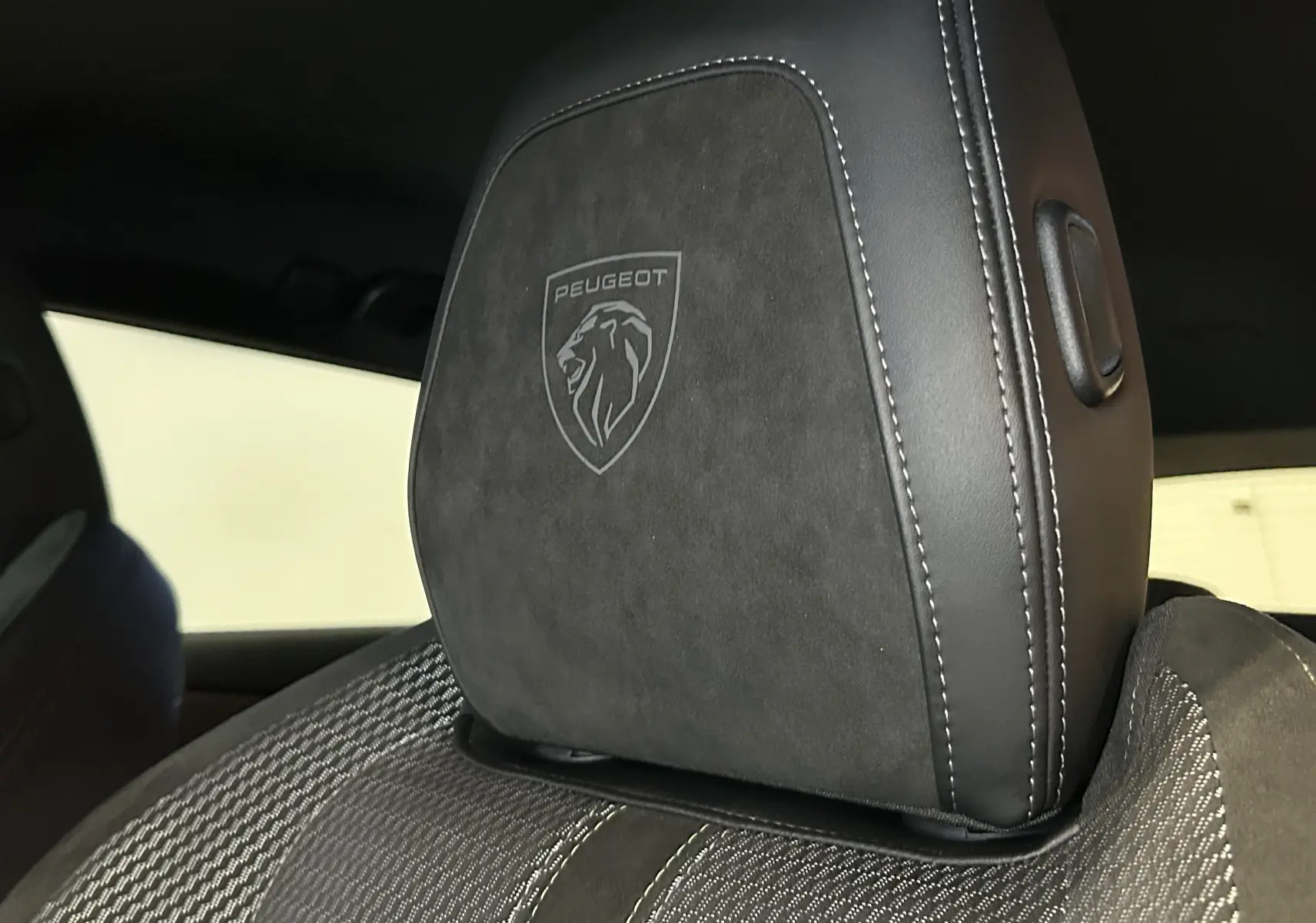 Gros plan sur l'appui-tête avant en cuir noir avec logo Peugeot embossé, intérieur de la 308 SW 2024.
