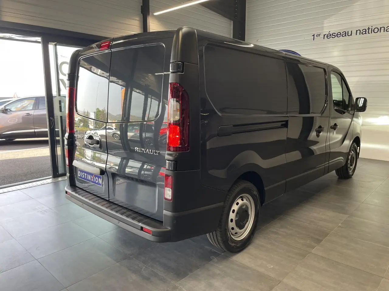 Renault Trafic Fourgon gris Comète vu en 3/4 arrière droit dans un showroom lumineux avec portes arrière fermées.