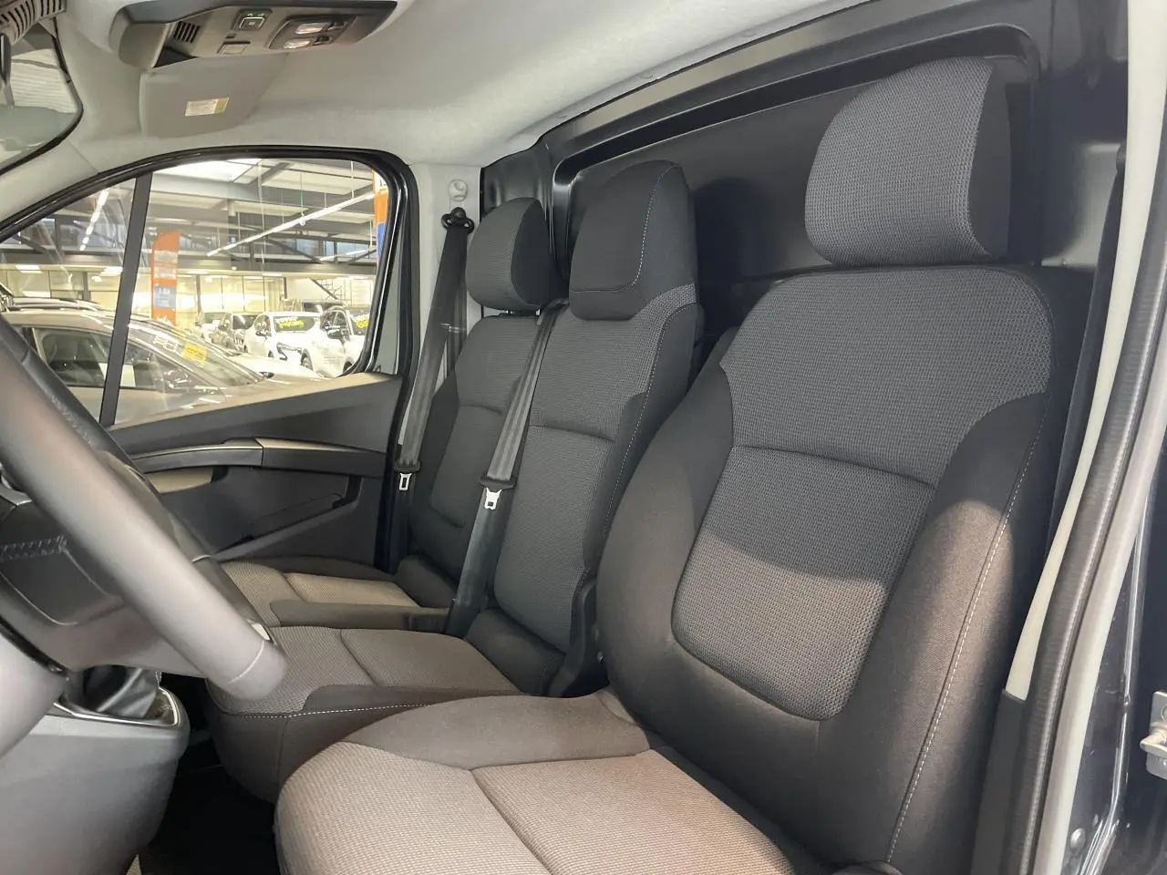 Vue intérieure côté conducteur du Renault Trafic Fourgon gris comète, montrant les sièges avant et la cloison tôlée arrière.