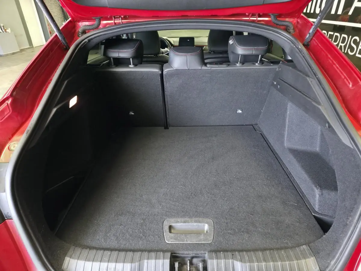 Coffre ouvert vu de l'arrière d'un Renault Arkana rouge, banquette arrière avec surpiqûres rouges visible.