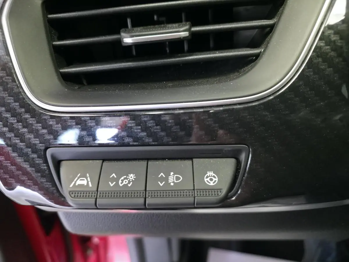 Gros plan sur les commandes d'assistance et réglages lumineux sur la planche de bord en carbone brillant du Renault Arkana Rouge Flamme.