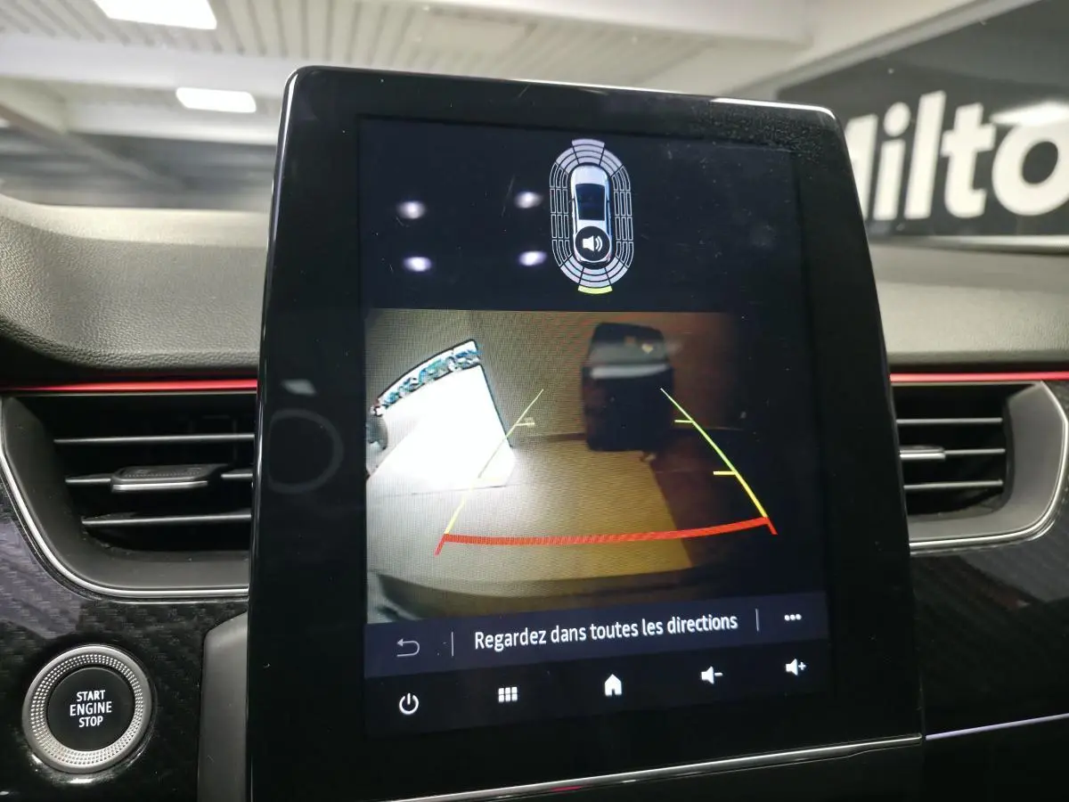 Écran tactile central montrant la caméra de recul du Renault Arkana R.S. Line, tableau de bord avec finition carbone et bandeau rouge.