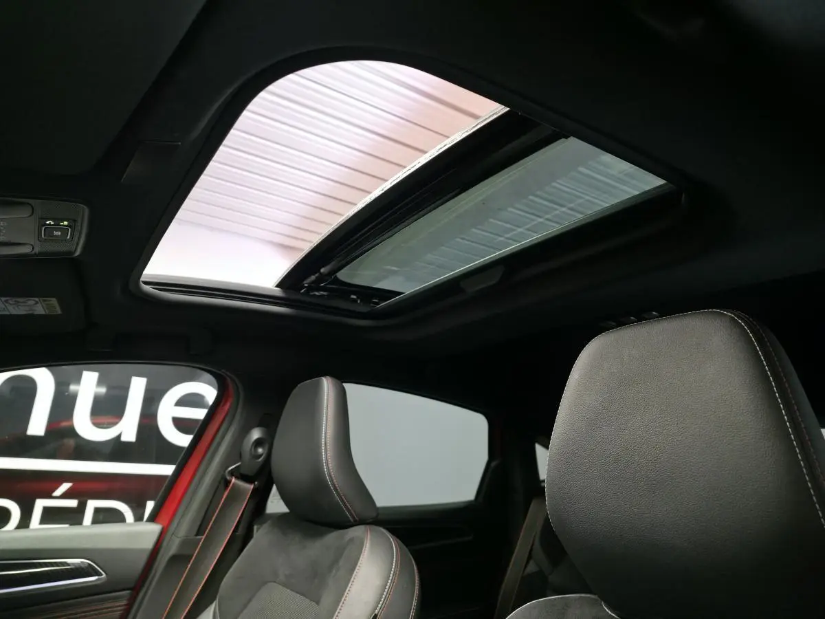 Intérieur du Renault Arkana rouge, vue sur les sièges avant en cuir noir avec surpiqûres rouges et toit ouvrant électrique.