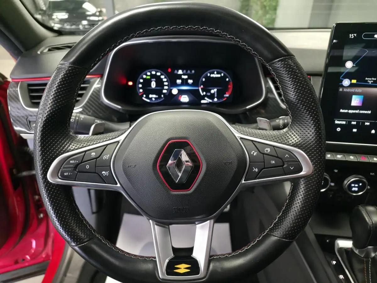 Volant sport en cuir perforé avec logo Renault encadré de rouge, tableau de bord numérique et écran tactile du Renault Arkana R.S. Line rouge.