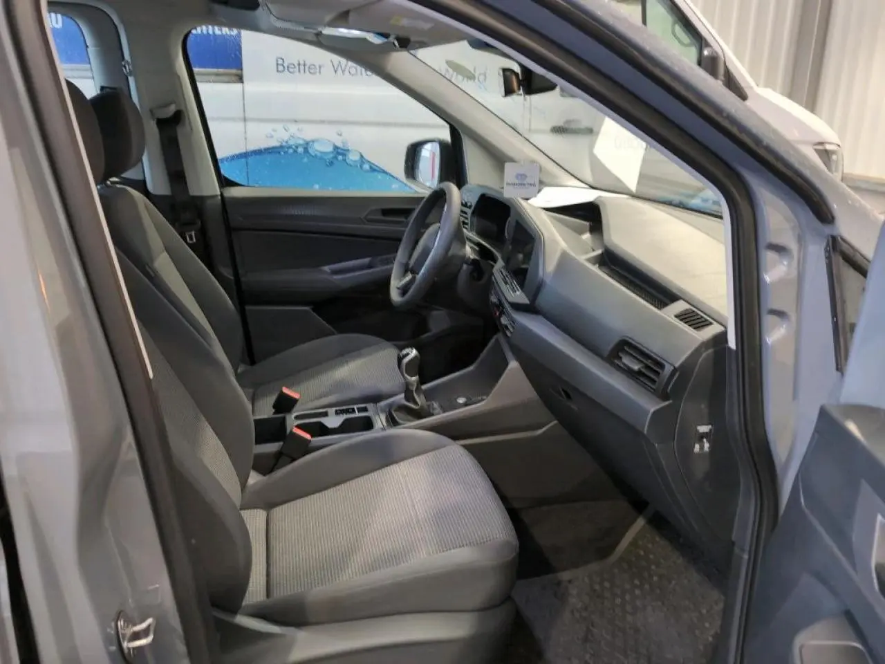 Vue intérieure côté conducteur du Volkswagen Caddy Maxi 2024 gris, montrant sièges et tableau de bord moderne.