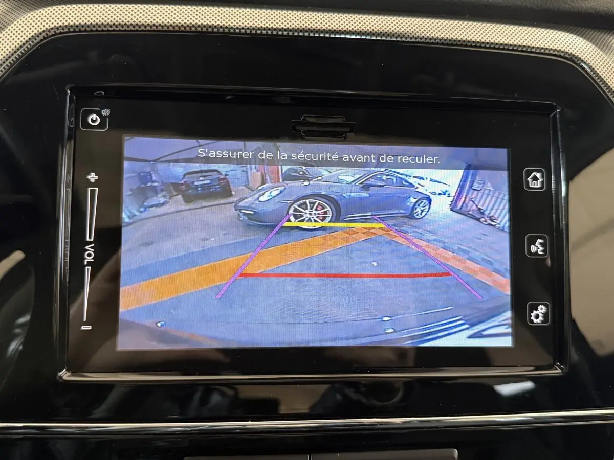 Écran tactile du Suzuki Vitara 2022 montrant la caméra de recul avec vue arrière sur un véhicule gris en garage.