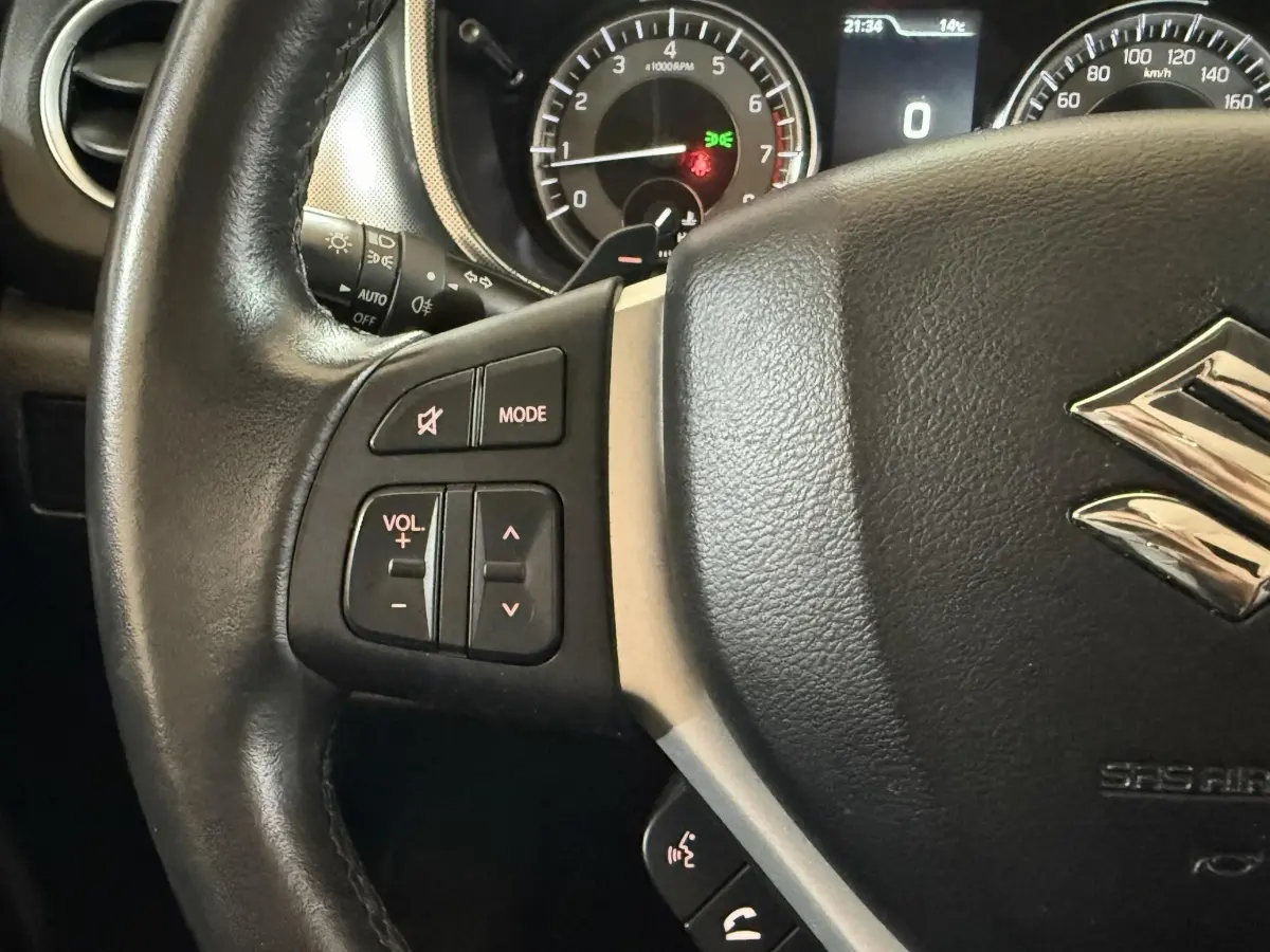 Gros plan sur le volant cuir et alu du Suzuki Vitara noir 2022, avec commandes audio et affichage du tableau de bord en arrière-plan.